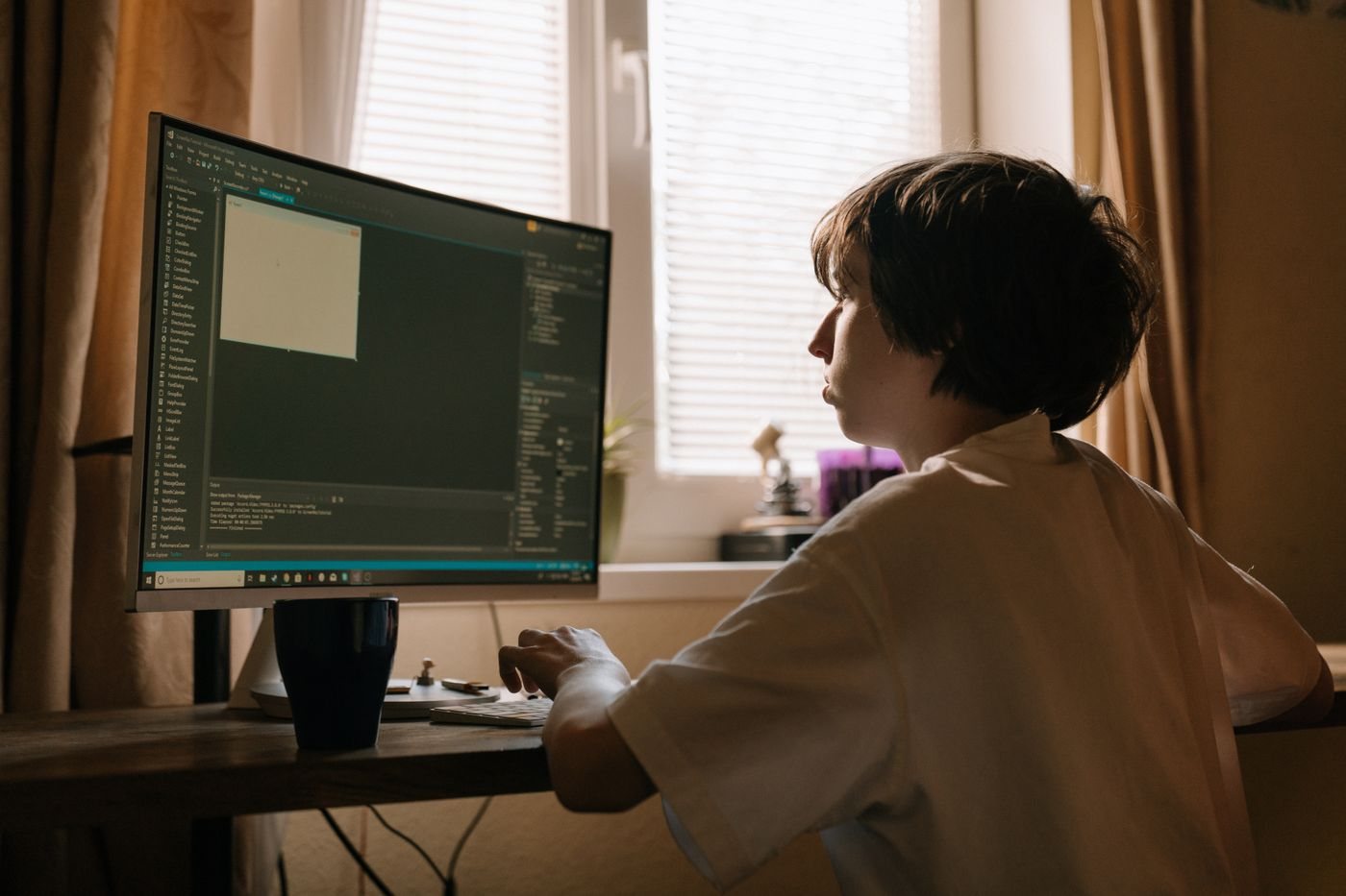 A boy writing code on a desktop computer at home